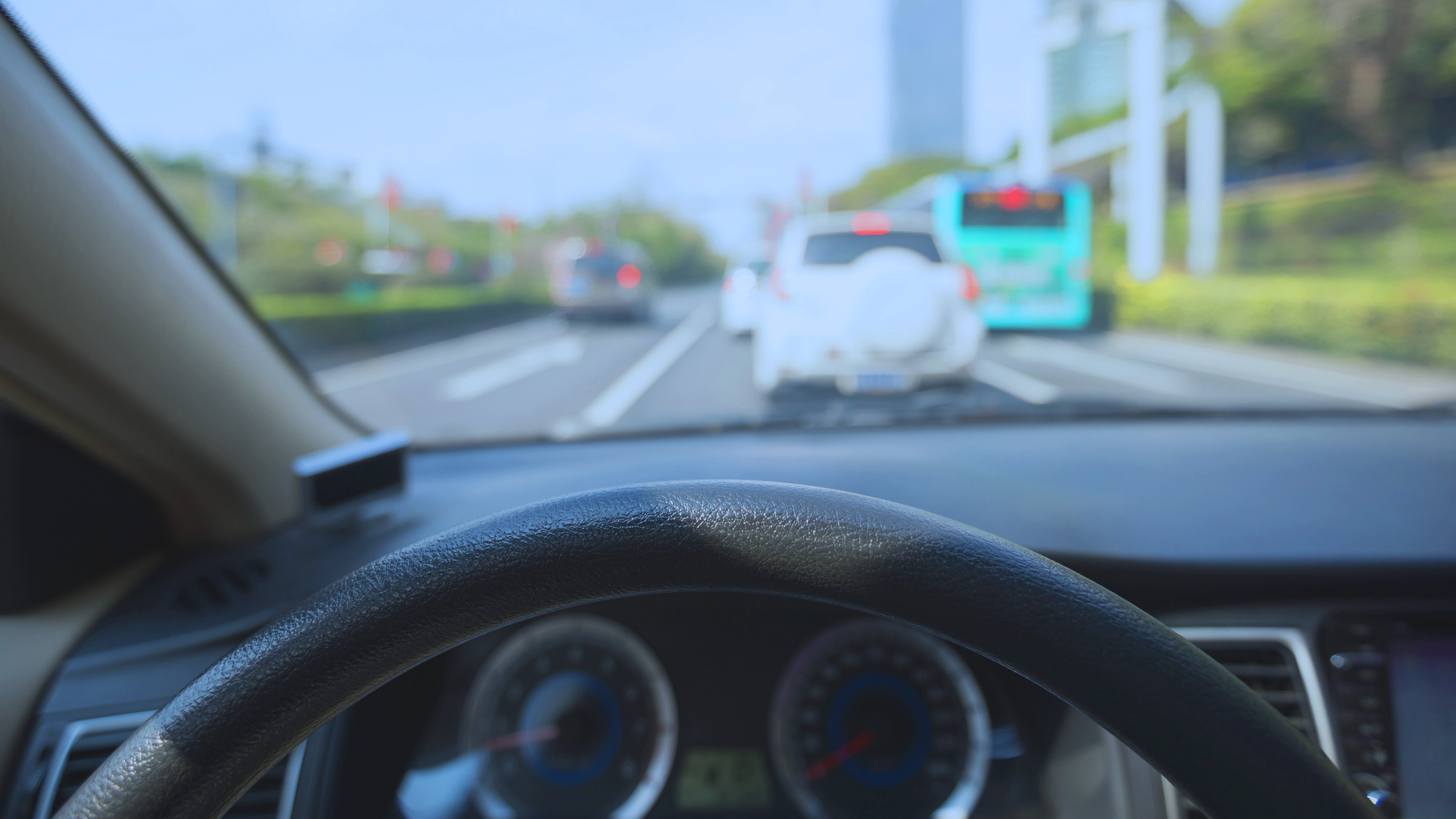 Photo of a car dashboard and top half of the steering wheel with traffic out the windshield