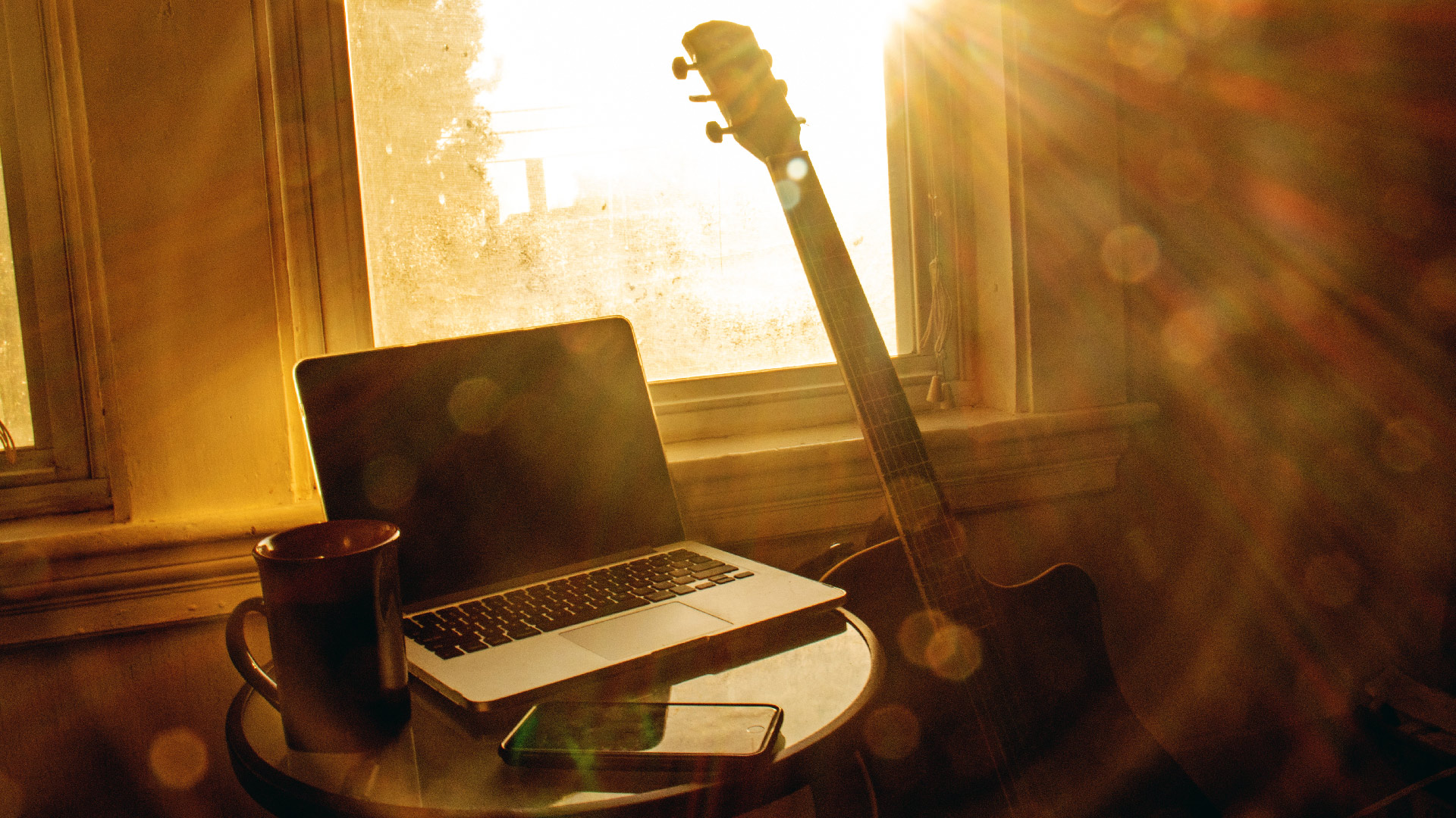 Morning table scene with smartphone, laptop, coffee, and guitar