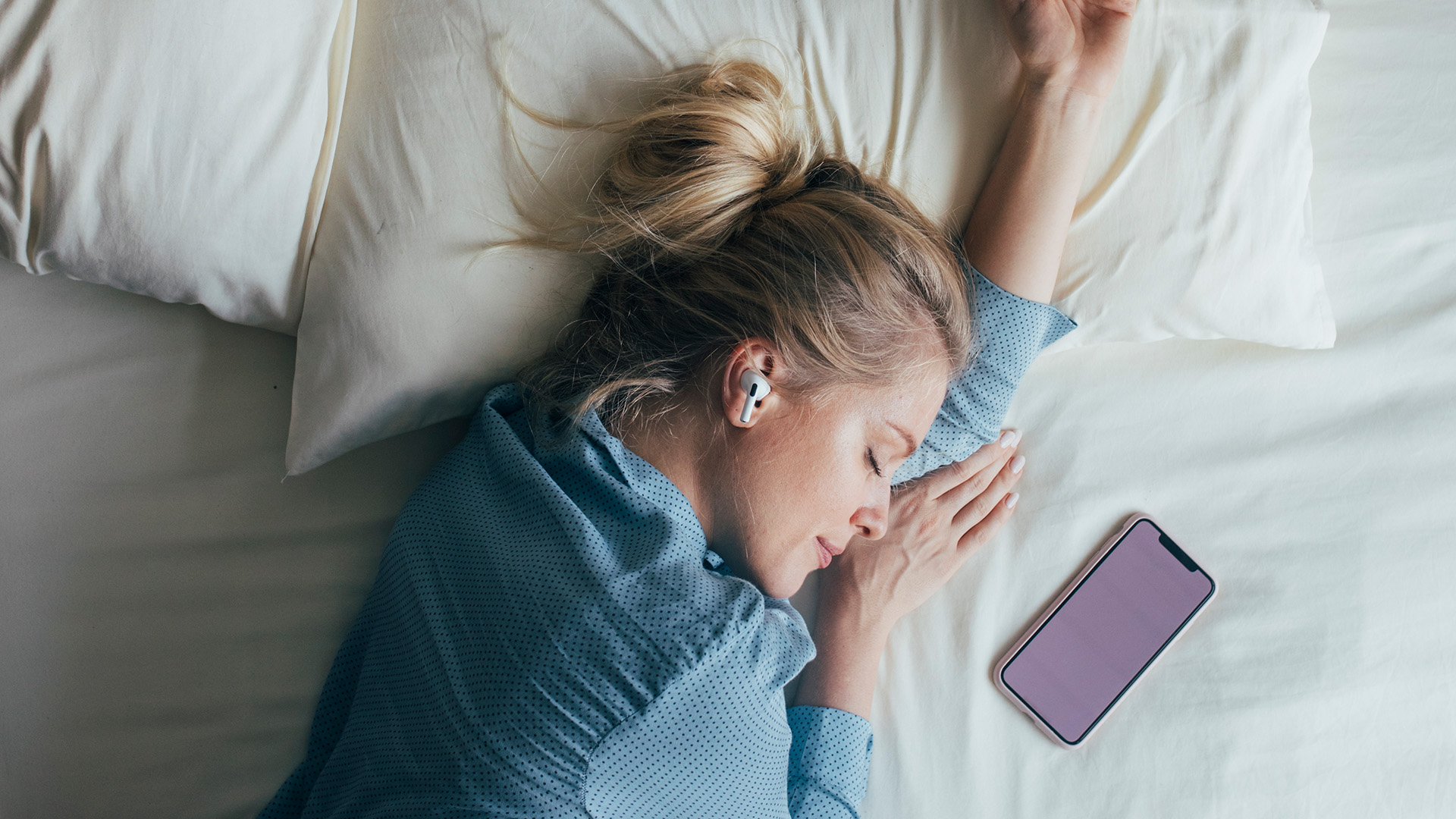 Woman in Pyjamas With Wireless Headphones Listening to Relaxing Music on Her Smartphone in Bed in the Morning - stock photo