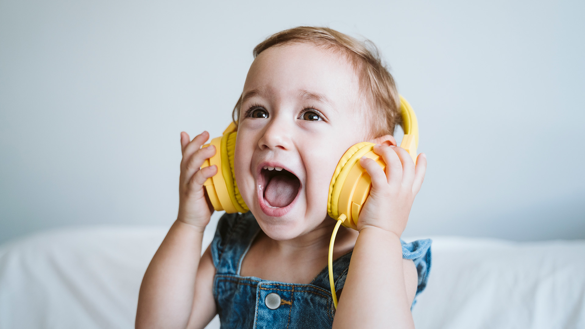 Baby girl at home listening to music on bed - stock photo